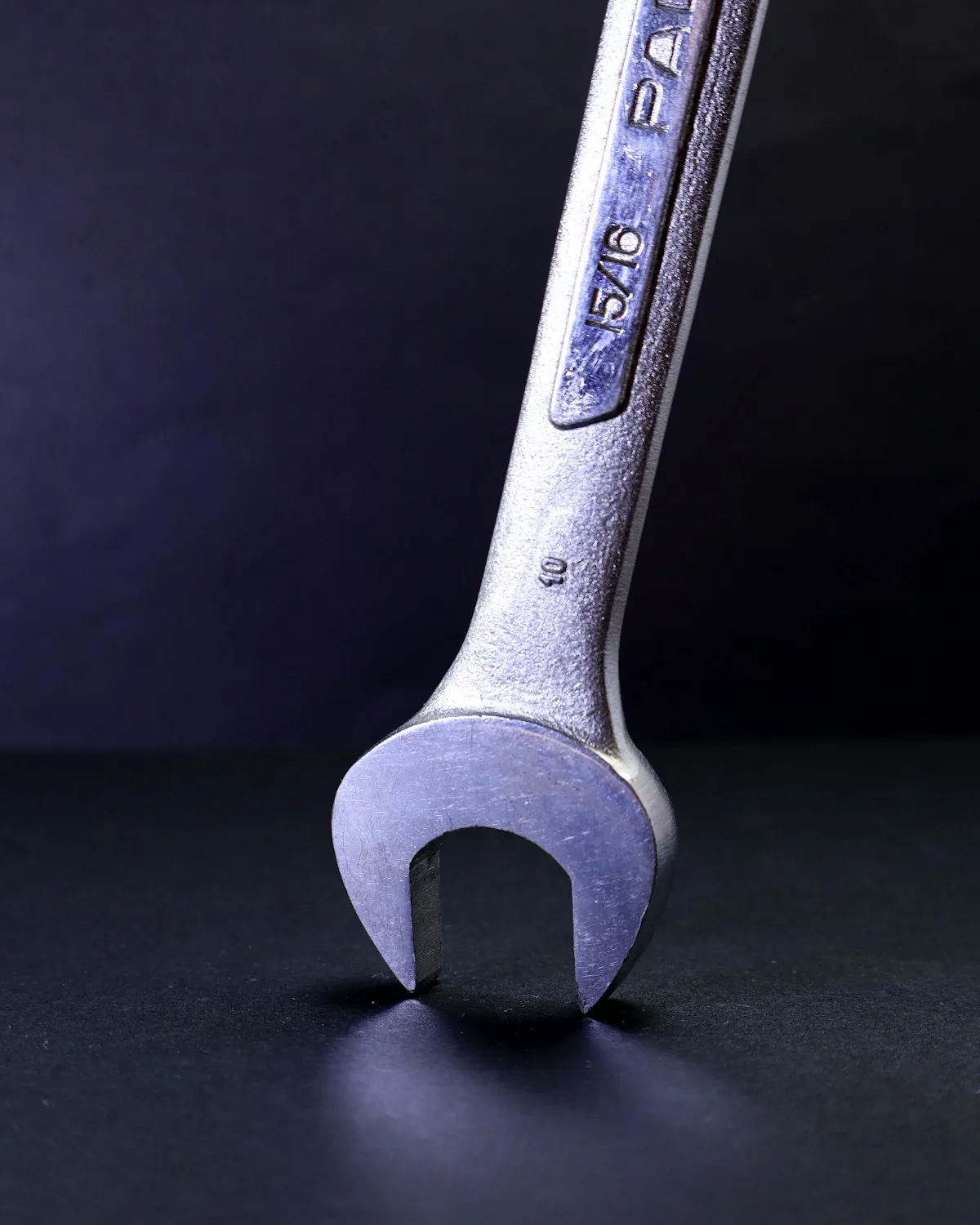 Llave combinada de acero cromado en primer plano, sobre fondo oscuro con luz azulada