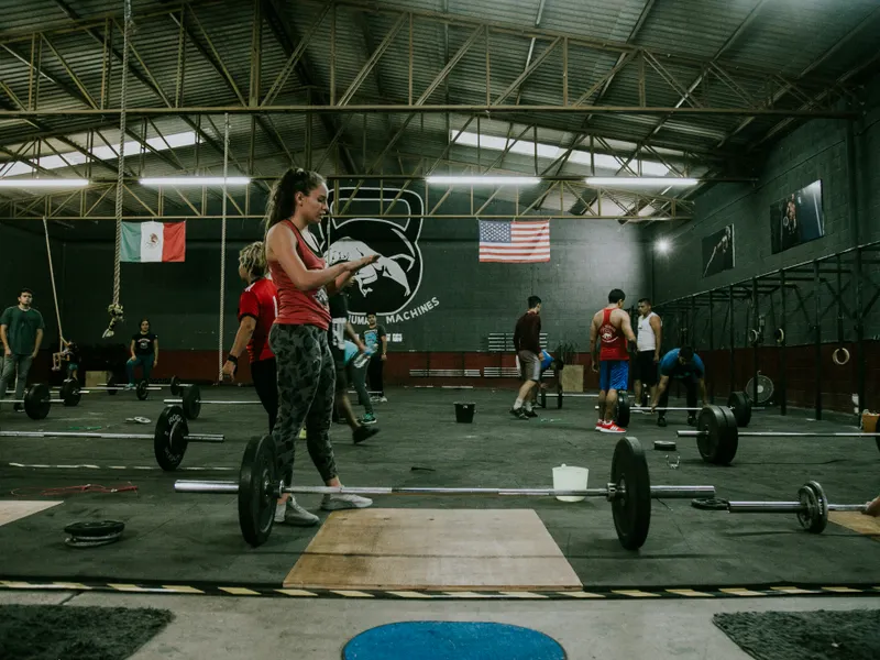 Grupo entrenando con barras olímpicas y discos en una sala amplia