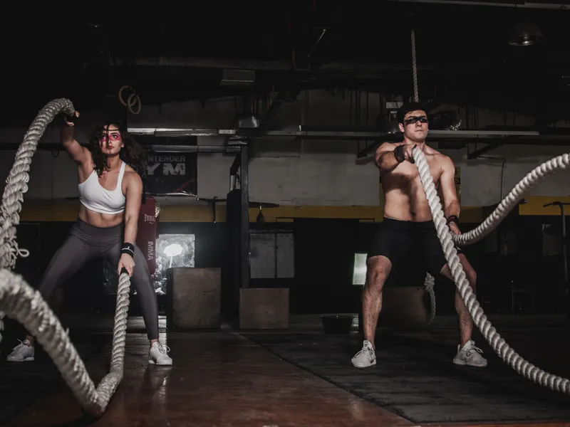 Dos personas entrenando con cuerdas de batalla en una sala oscura