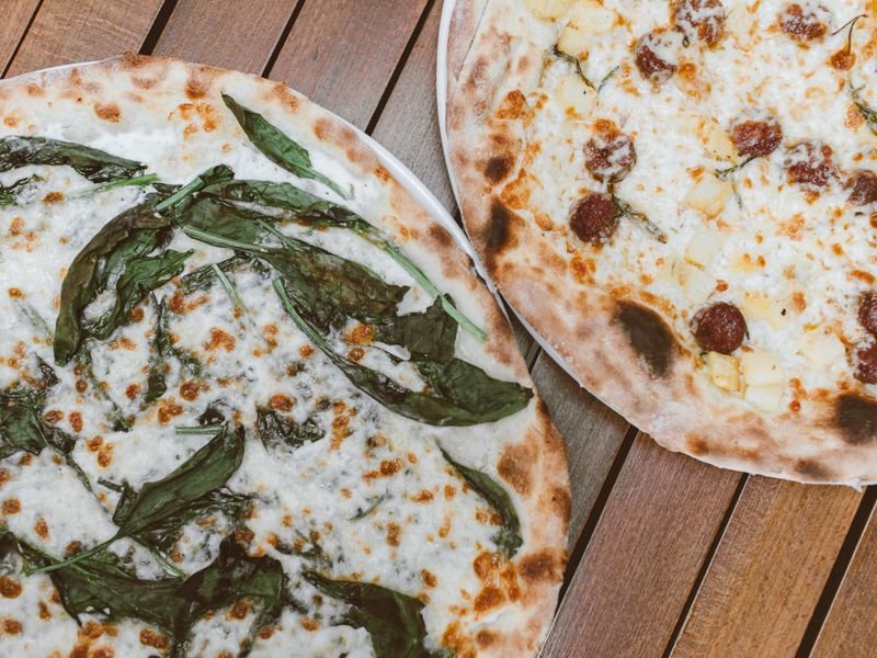 Dos pizzas con distintos gustos sobre mesa de madera