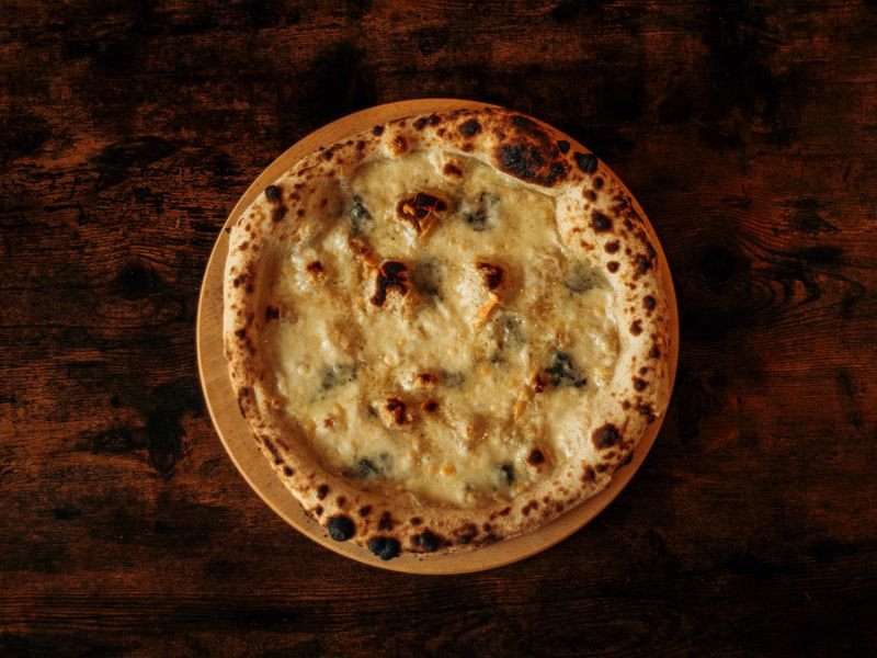 Pizza cuatro quesos gratinada sobre mesa de madera